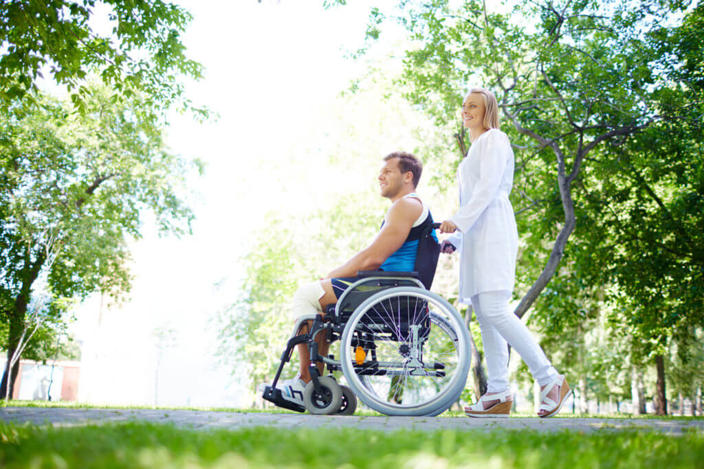 Pretty nurse walking with male patient in a wheelchair in park